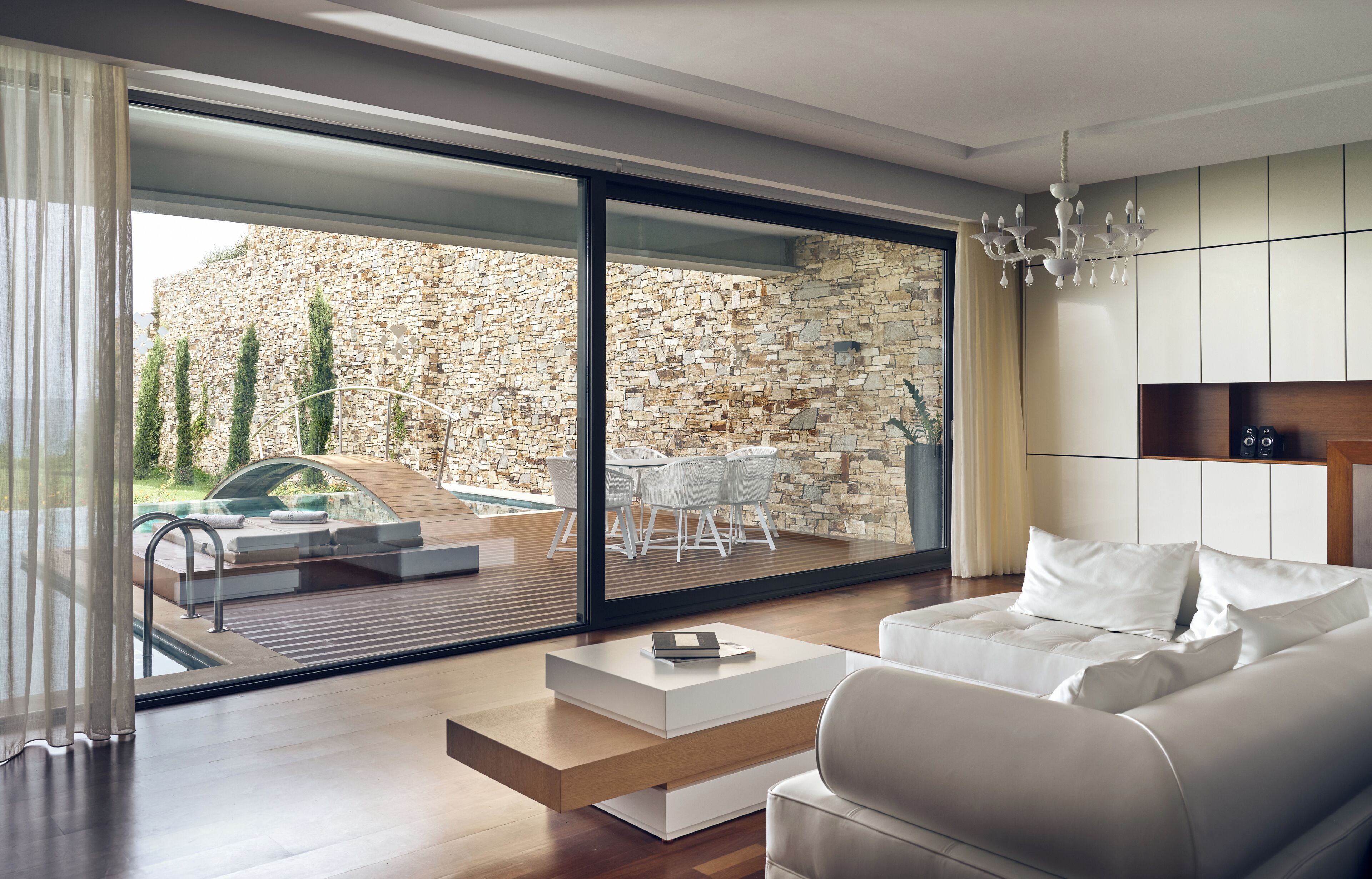 Un salón moderno con sofá, mesa de centro y vistas a un patio exterior con piscina y pared de piedra.
