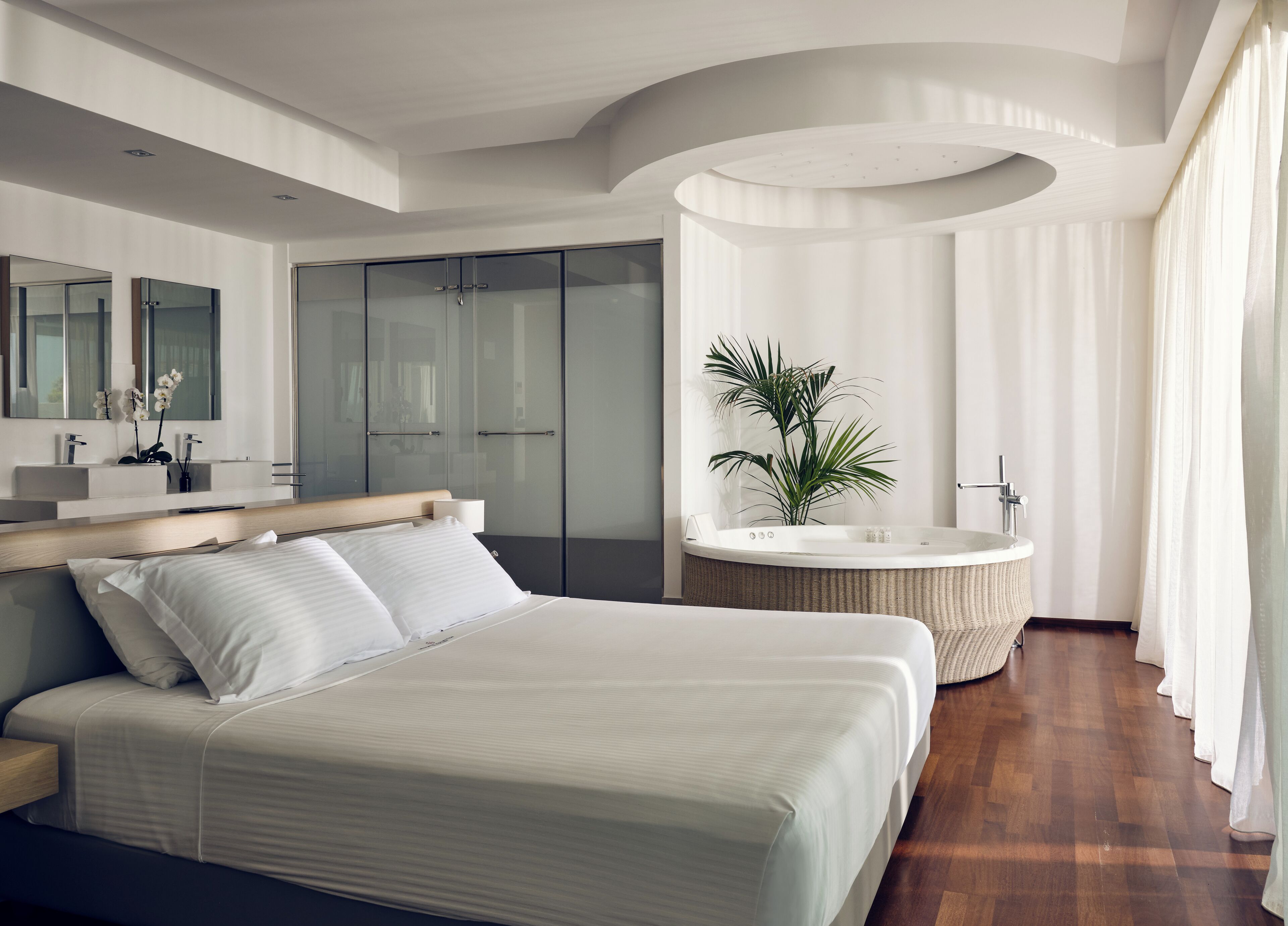 Un dormitorio moderno con una cama grande, un tocador con espejo, un vestidor y una bañera independiente.