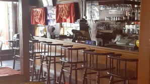 En restaurant med træborde og stole, et barområde med en tv-skærm og en ventilator i loftet.