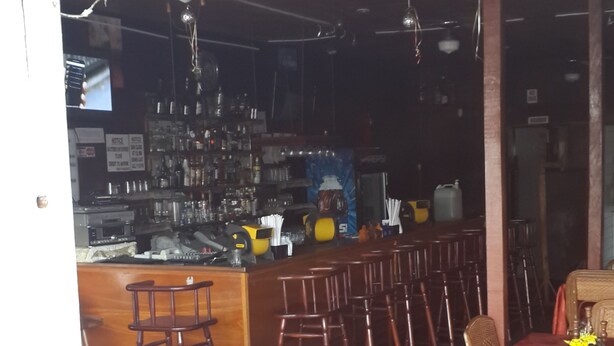 En restaurant med fletstole og borde, et barområde, og et skilt der viser, at det er et pensionat åbent døgnet rundt.