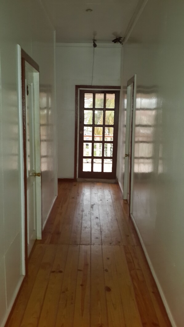 Un corridoio con pavimento in legno, pareti bianche e una porta che dà su uno spazio all'aperto con vista sul verde.