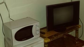 A room with a microwave, a television on a wooden stand, and a bed.
