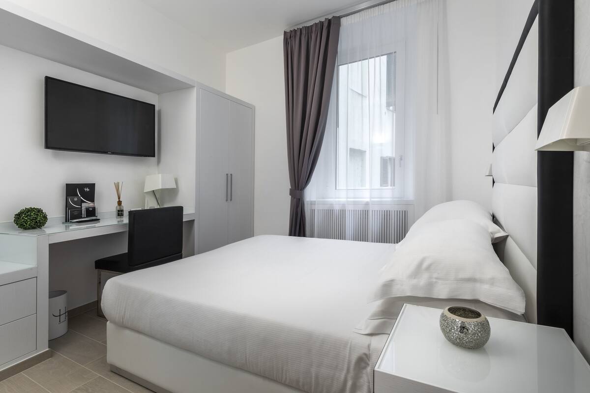 Quarto de hotel moderno com uma cama grande, uma escrivaninha com computador, televisão de tela plana e janela com cortinas.