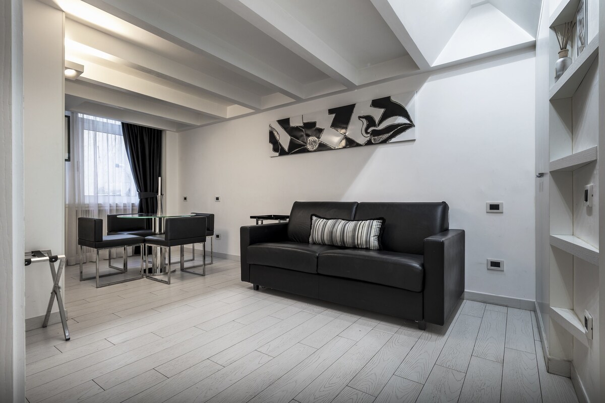 A modern living room with a black leather sofa, a glass coffee table, and a contemporary abstract art piece on the wall.
