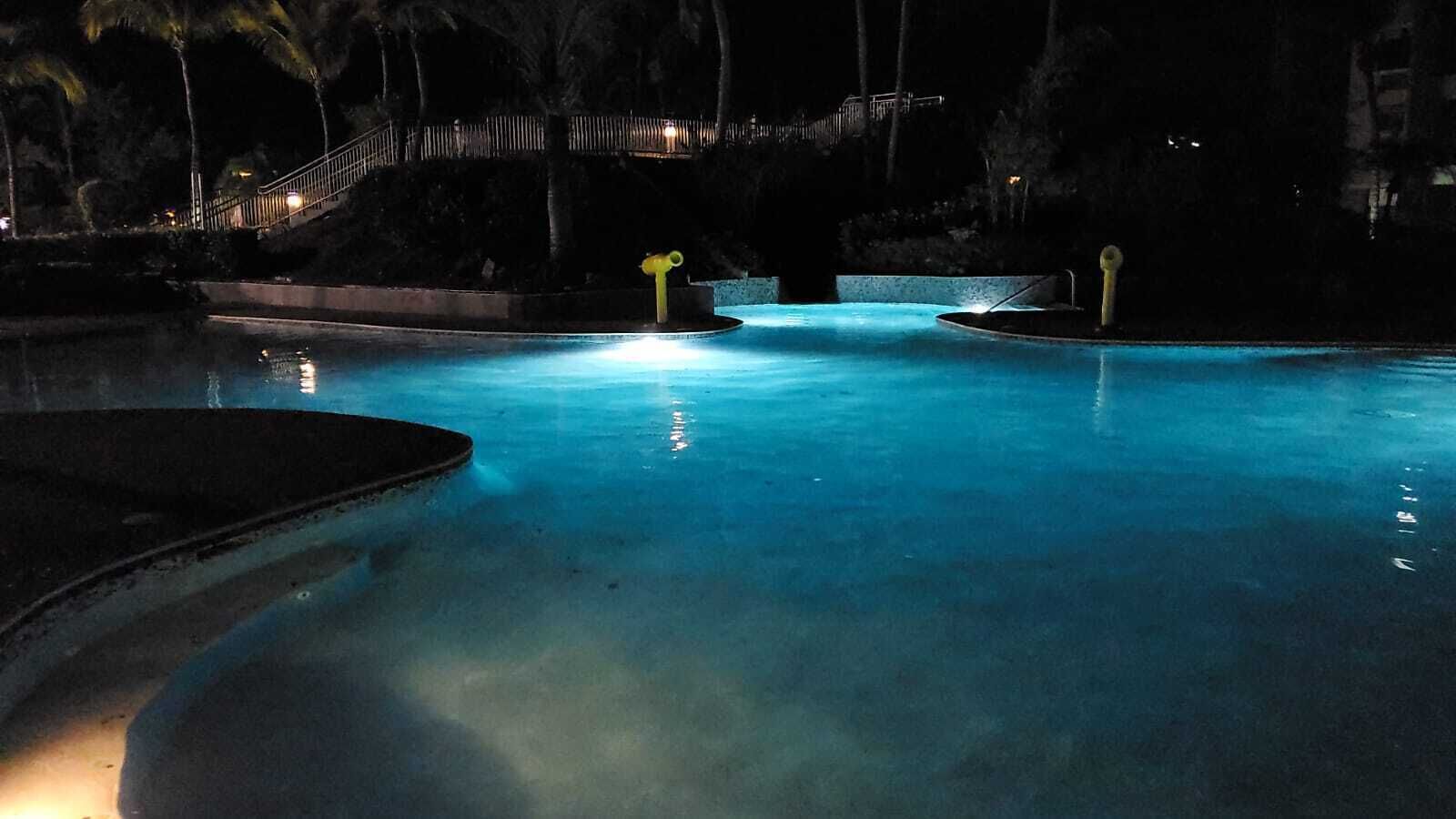 A nighttime swimming pool with a curved edge and a central island.