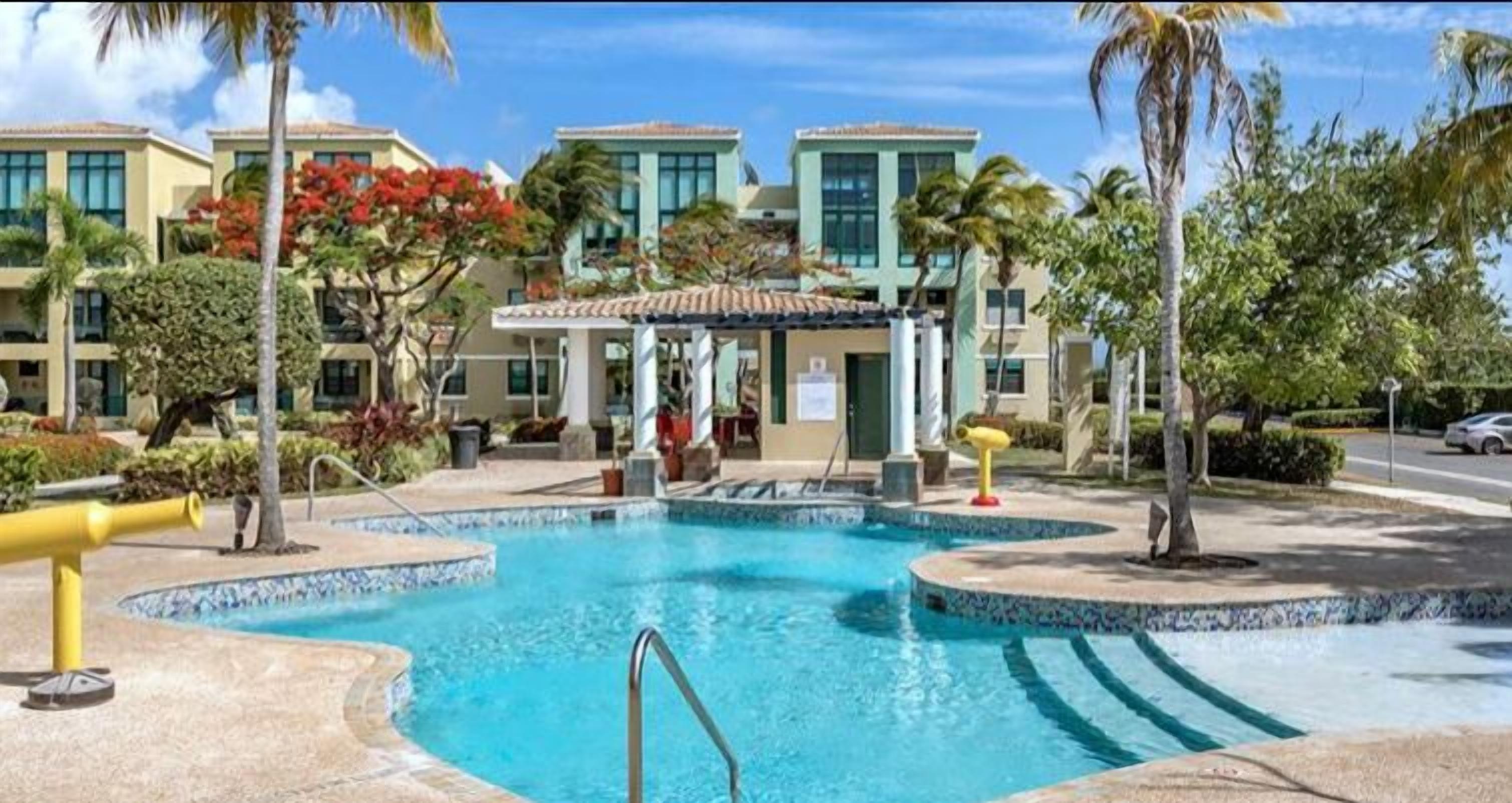 A swimming pool with a tiled edge, surrounded by palm trees and a covered seating area.