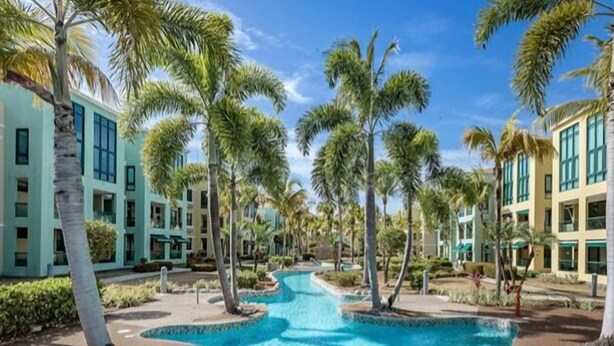 Un resort con piscina central, palmeras y edificios modernos.