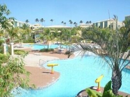 Zona de piscina en un resort con varias piscinas, palmeras y cielo despejado.