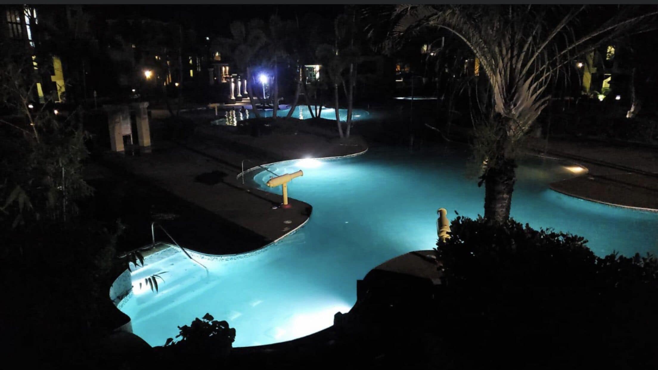Vista noturna de uma área de piscina com várias piscinas, iluminada por iluminação artificial.
