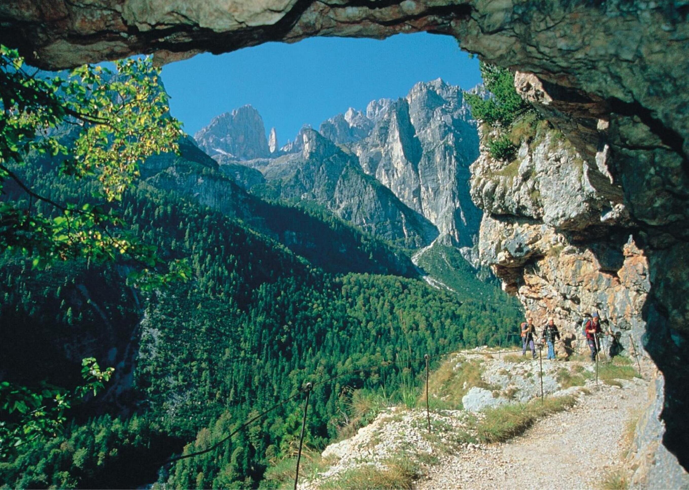 A mountainous landscape with a rocky overhang and a group of hikers on a trail.