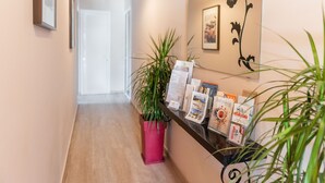 Un espace d’accueil doté d’un plancher en bois, d’une plante rose et d’un comptoir noir où sont disposées des brochures et une photo encadrée au mur.