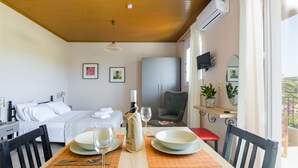 Une chambre d’hôtel avec un lit, une table à manger dressée avec des assiettes, des verres et une bouteille, une chaise, un téléviseur fixé au mur et une fenêtre donnant sur un paysage.