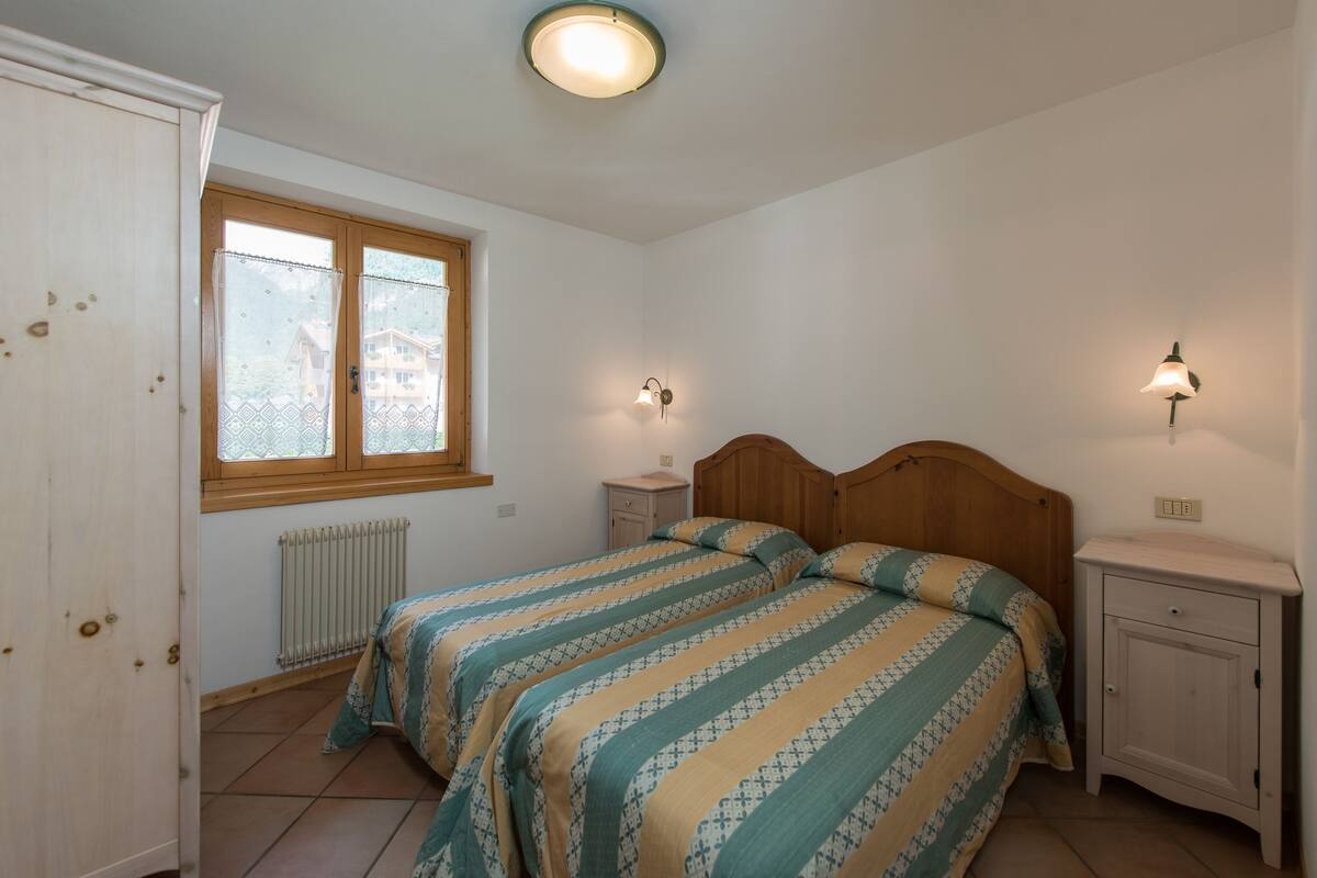 A bedroom with two beds, a window, a radiator, and bedside lamps.