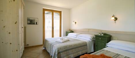 A bedroom with two beds, a wooden wardrobe, a green nightstand, and a wall-mounted light fixture.