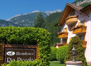 Un hotel con un cartel que dice "Residence Rio Pigolo", rodeado de vegetación exuberante y montañas al fondo.