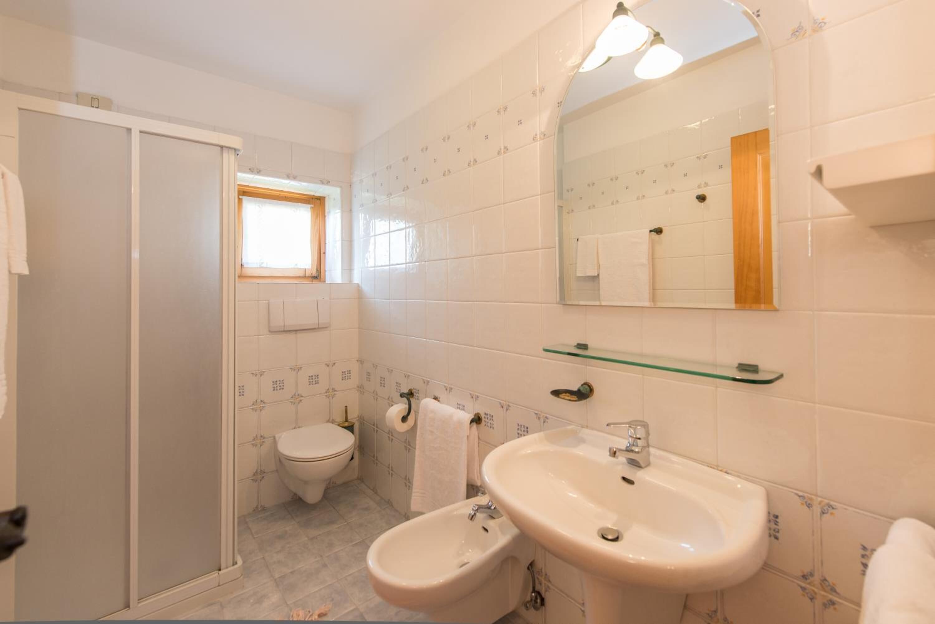 Et badeværelse med toilet, bidet, vask og spejl.