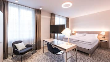 Una habitación de hotel con cama, escritorio, silla, televisor y mesita de noche con lámparas.