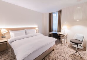 Una habitación de hotel con una cama grande, un escritorio, una silla y una lámpara.