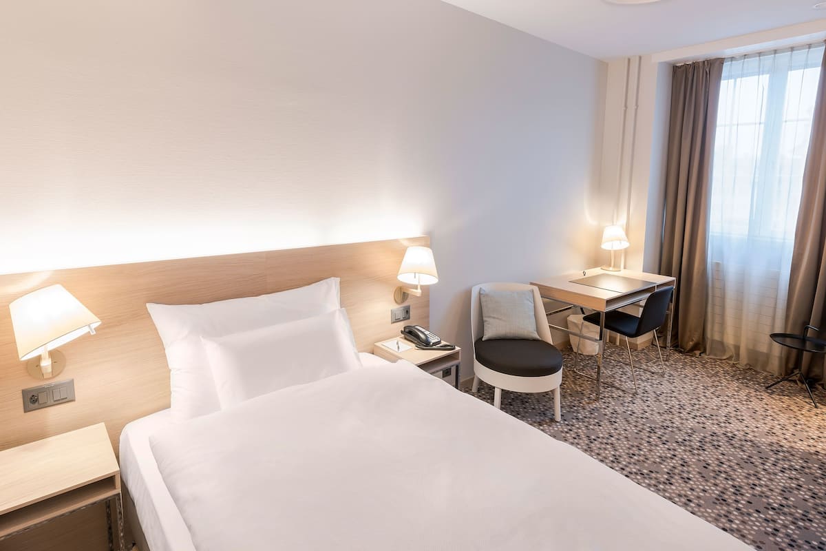A hotel room with a bed, desk, chair, and a telephone.