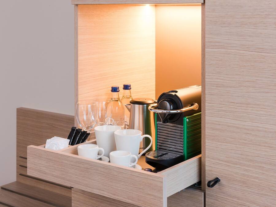 A wooden drawer with a coffee machine, cups, and bottles.