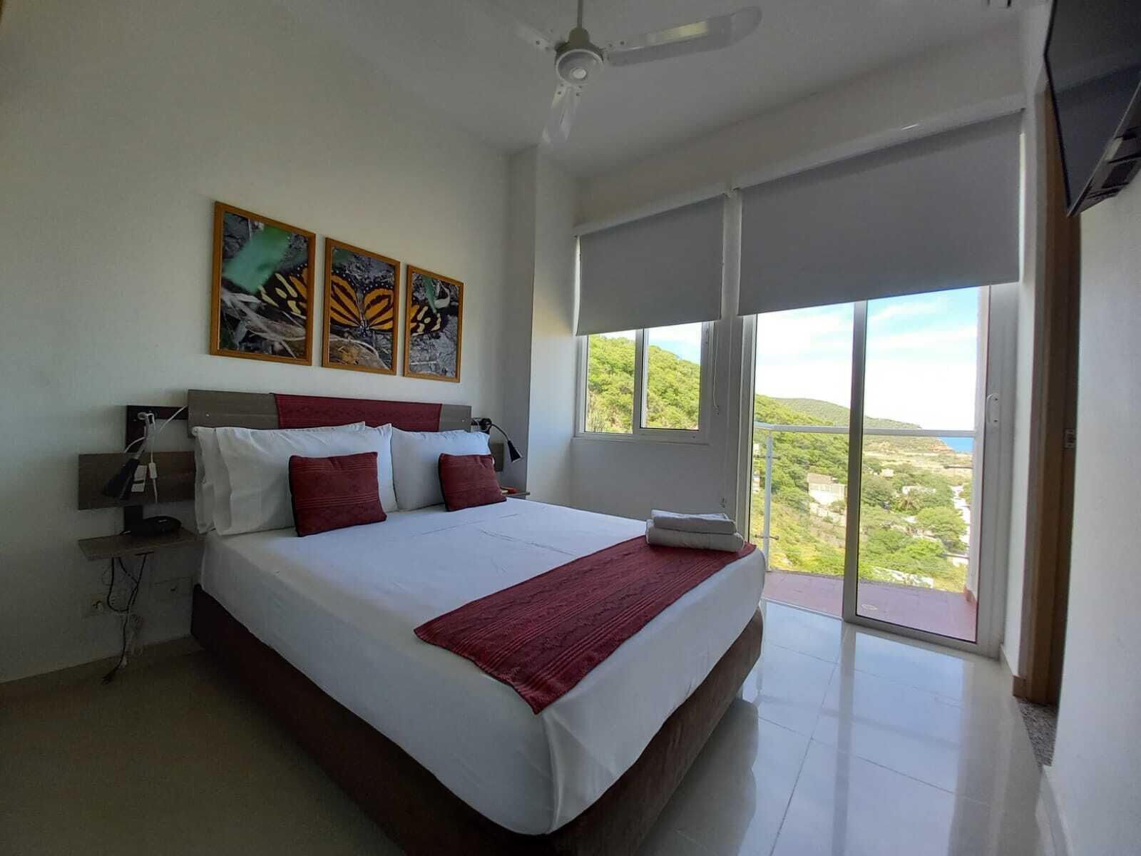 A spacious bedroom with a large bed, a ceiling fan, and a balcony with a scenic view.