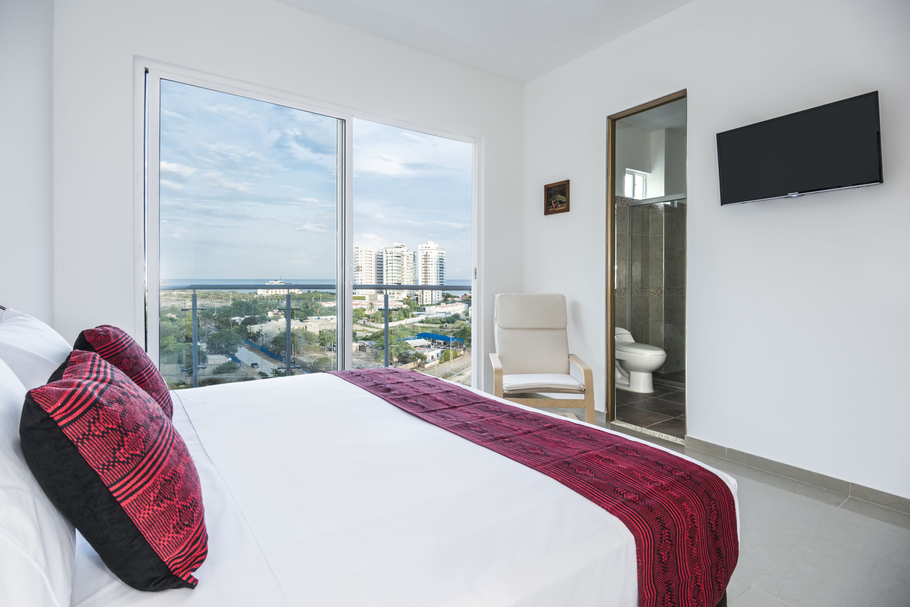 A hotel room with a large bed, a chair, a toilet, and a TV mounted on the wall.