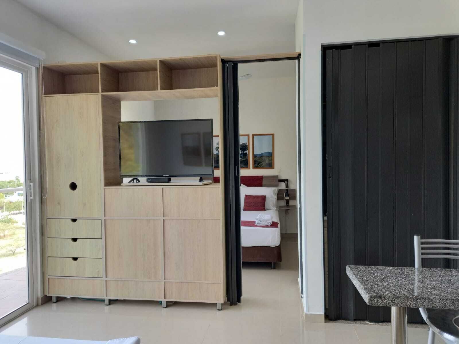 A modern bedroom with a built-in wardrobe, a flat-screen TV, and a bed with a red accent.