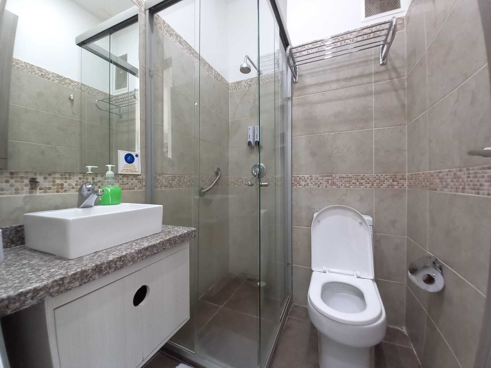 Un bagno moderno con box doccia in vetro, lavabo bianco con erogatori di sapone e water.