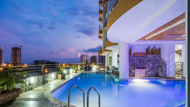 A swimming pool with a stone wall and a view of the city skyline at dusk.