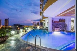 A swimming pool with a stone wall and a view of the city skyline at dusk. - Terrazas Tayrona Travelers Apartamentos y Suites (Santa Marta)