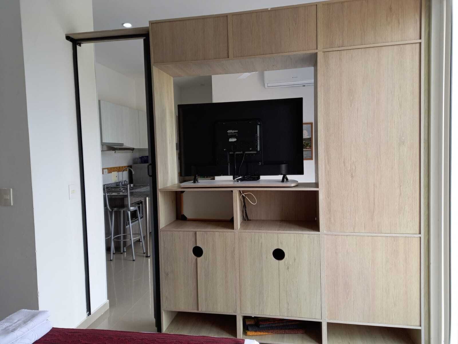 A compact room with a kitchenette, a TV on a stand, and a sliding door leading to another area.