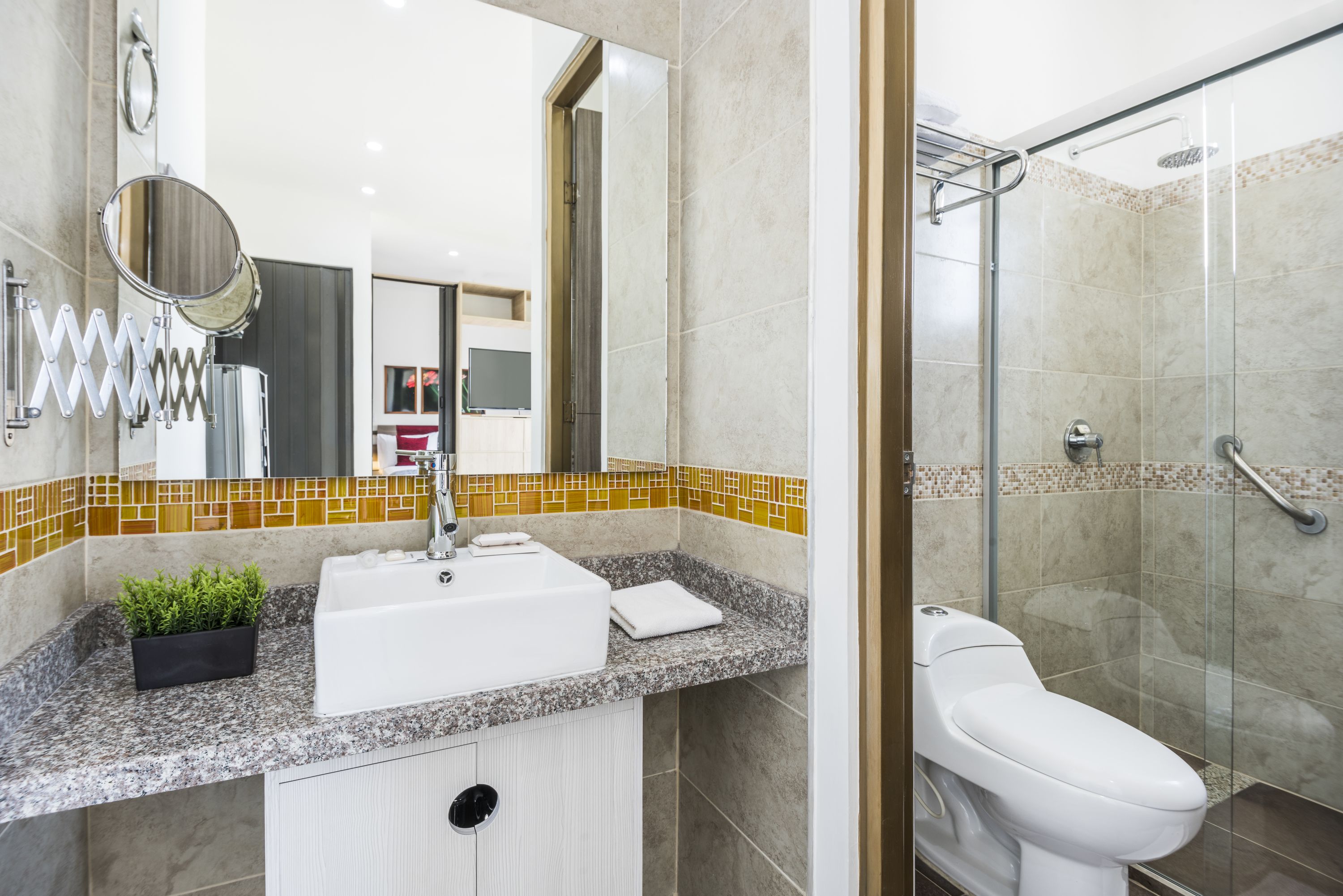 Ein modernes Badezimmer mit Granitplatte, weißem Waschbecken, einer Duschkabine aus Glas und einer Toilette.