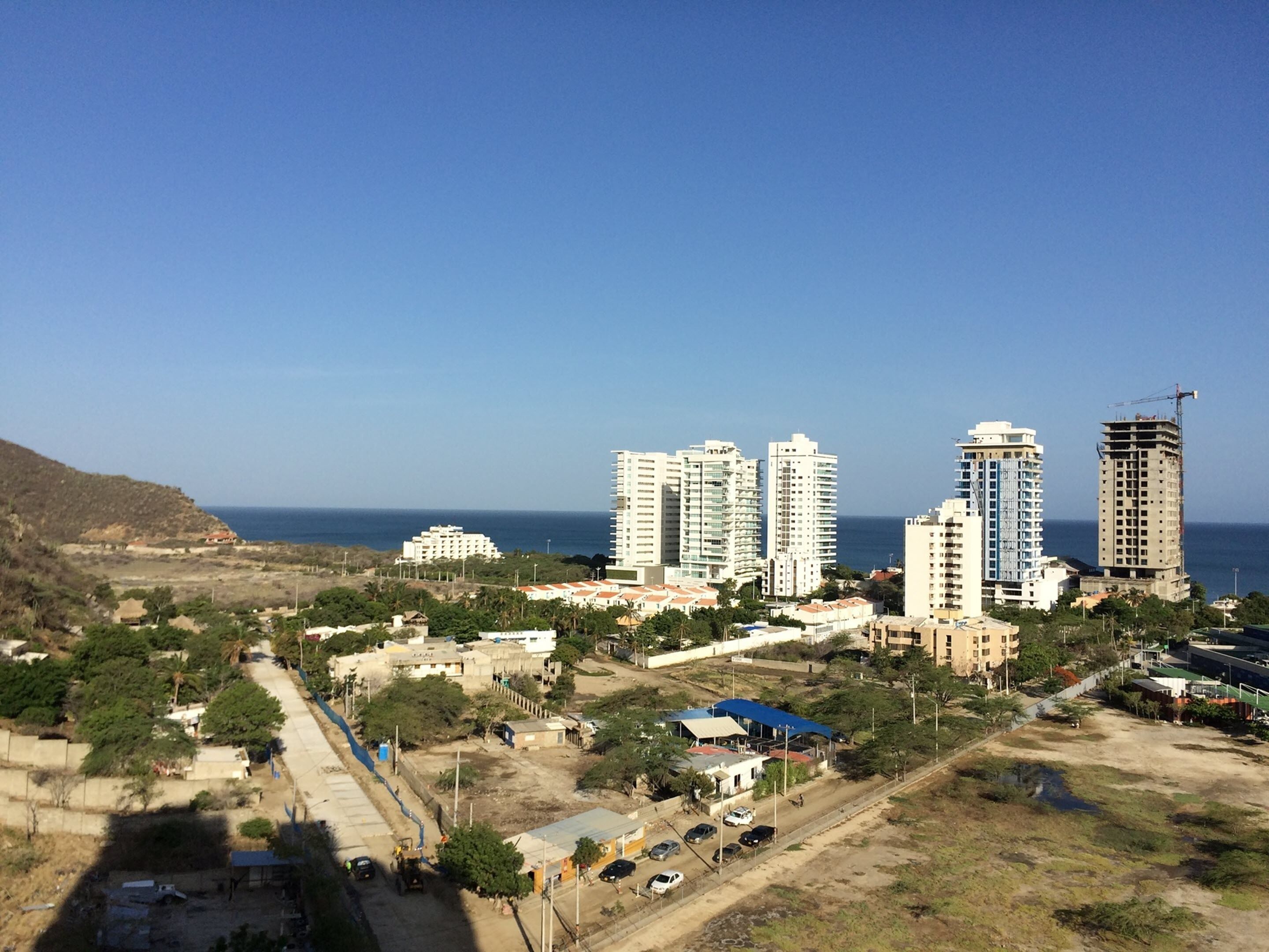 A coastal cityscape with high-rise buildings, a construction site, and a clear view of the sea.
