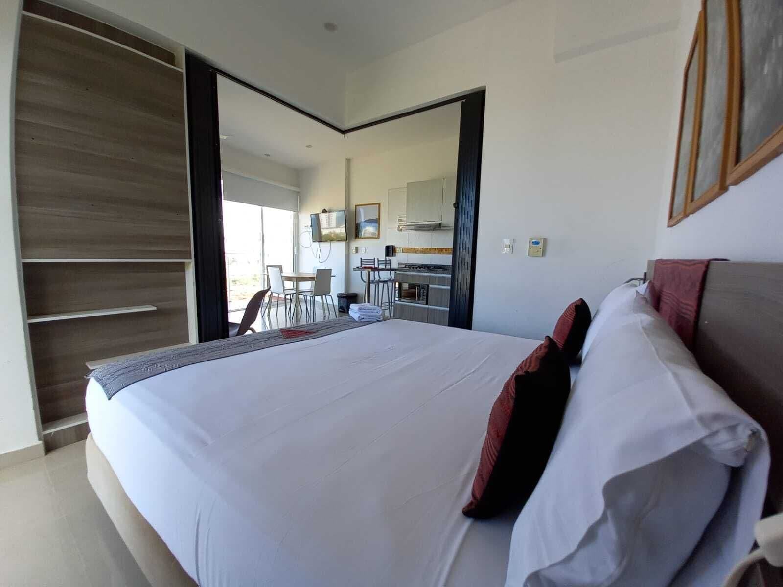 Une chambre d’hôtel avec un grand lit, un bureau et, au fond, une petite cuisine.