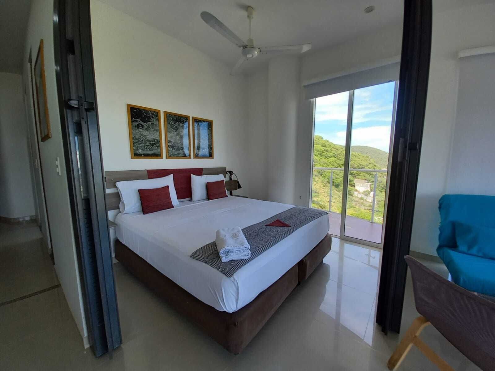 Un dormitorio moderno con una cama grande, un ventilador de techo y un balcón con vistas.