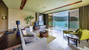 A modern hotel room with a sofa, coffee table, TV, and a balcony with a view of the sea. - Impiana Private Villas (Phuket)