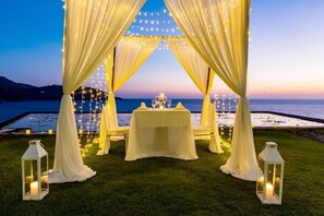 An outdoor wedding setup with a table and chairs, draped curtains, string lights, and lanterns. - Impiana Private Villas (Phuket)