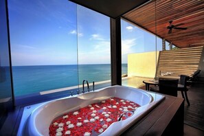 A modern bathroom with a large bathtub filled with water and floating flowers, overlooking a clear blue sea. - Impiana Private Villas (Phuket)