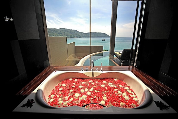 A large bathtub filled with water and red flowers, with a view of a pool and mountains in the background. - Impiana Private Villas (Phuket)