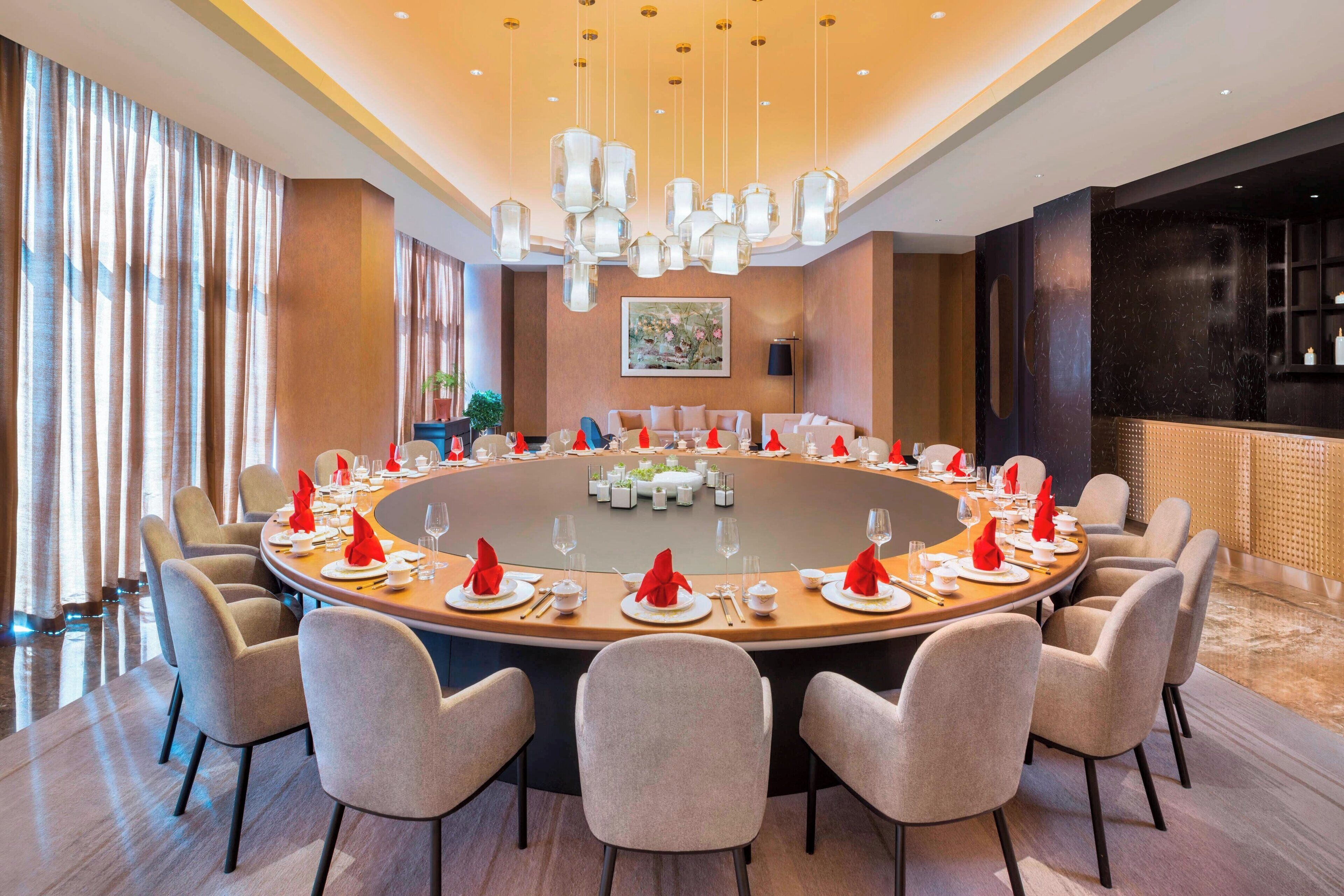A round table set for a meal with chairs around it, a painting on the wall, and a bar area in the background.