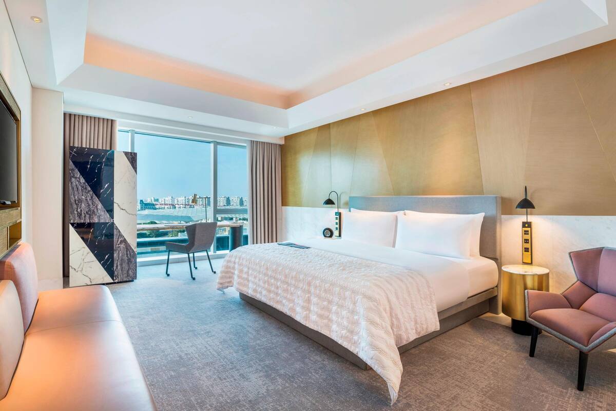 A modern hotel room with a large bed, a seating area, and a view of the city.