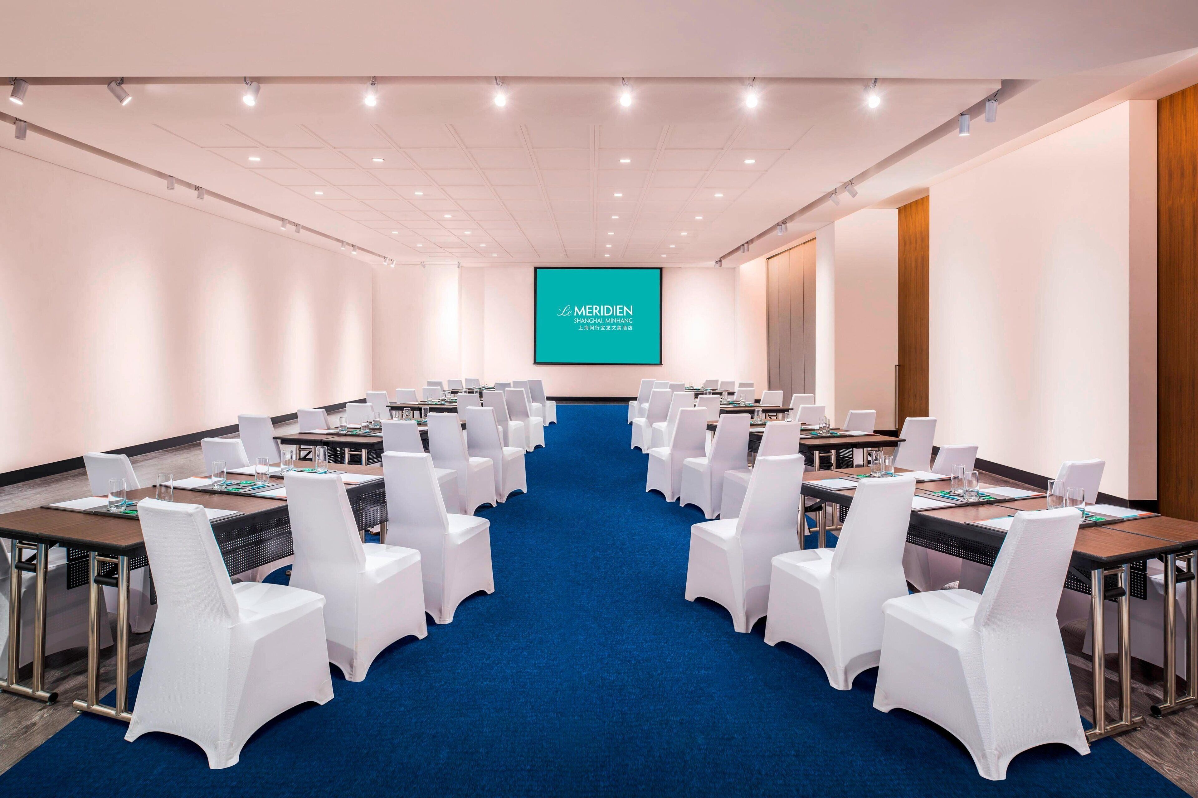 A conference room with a blue carpet, white chairs, and tables.