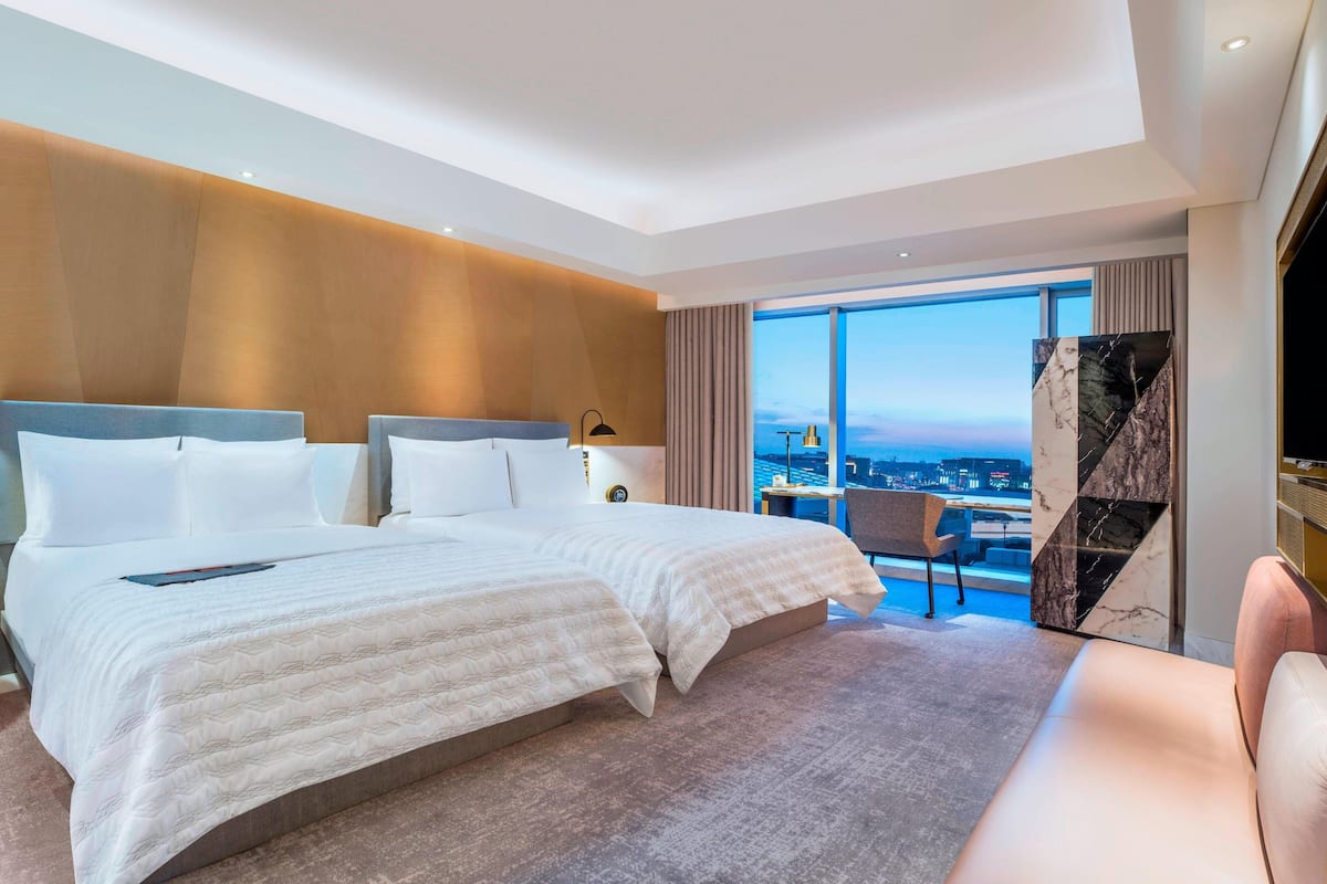A modern hotel room with a large bed, a sofa, and a city view.
