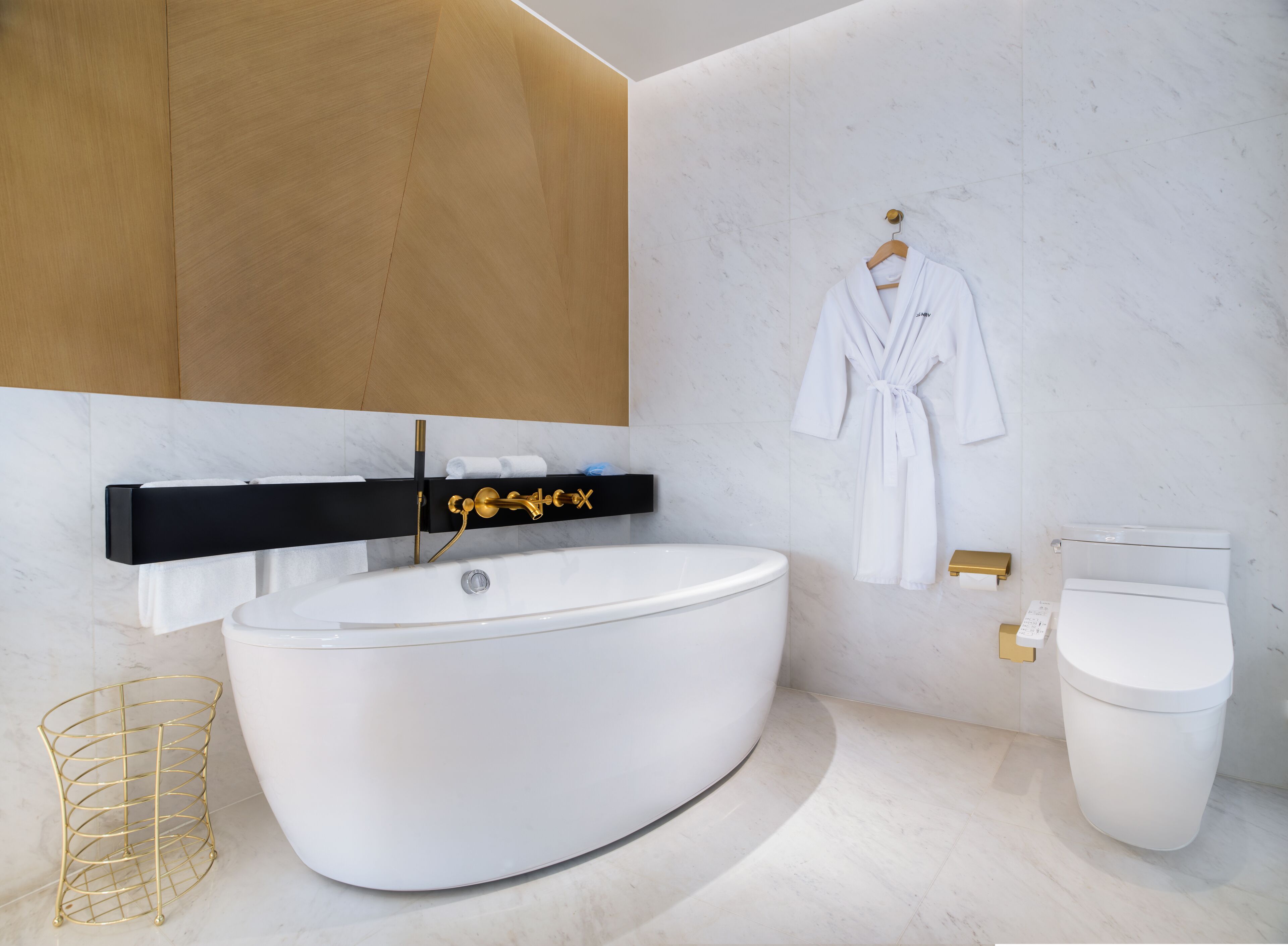 A modern bathroom with a freestanding bathtub, a gold-framed vanity, a white toilet, and a robe hanging on the wall.