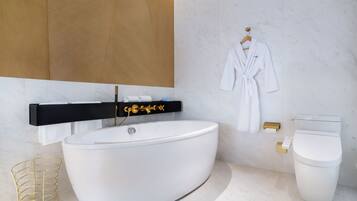 A modern bathroom with a freestanding bathtub, a gold-framed vanity, a white toilet, and a robe hanging on the wall.