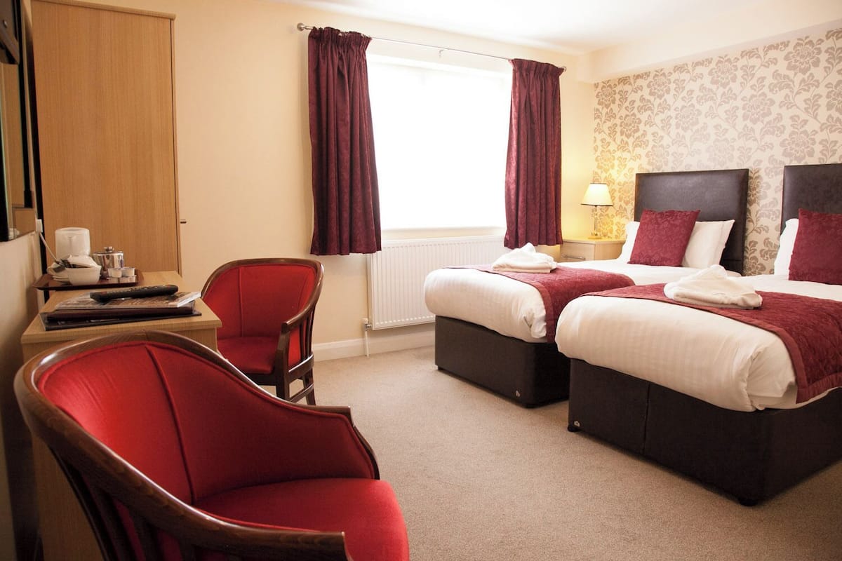 A hotel room with two beds, a desk, a chair, and a radiator.