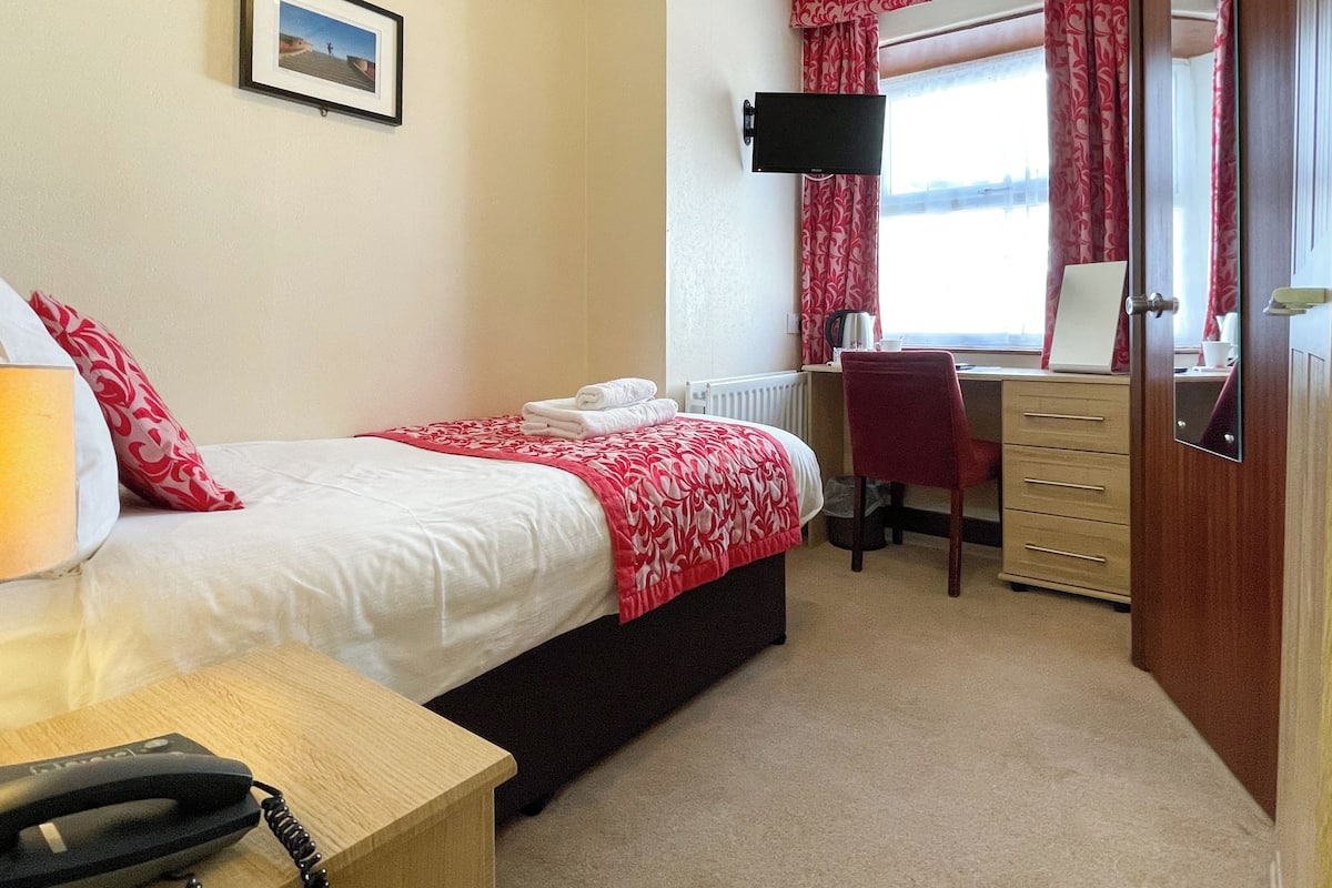 A hotel room with a bed, a desk, a chair, a TV, and a window with curtains.