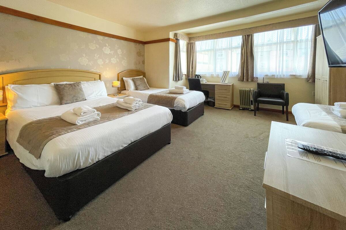 A hotel room with two beds, a desk, a chair, and a TV.