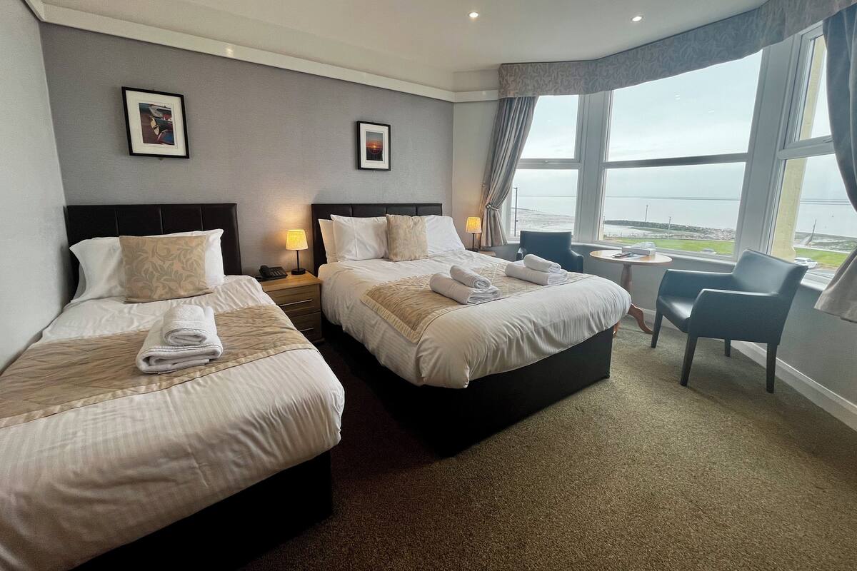 A hotel room with two beds, a small table, and a view of the sea.