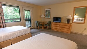 A hotel room with two beds, a desk with a chair, a television, a dresser, and a window with a view of trees.